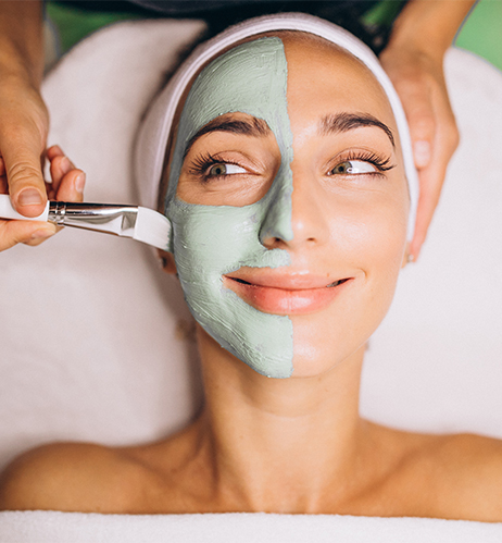 Esthetician applying facial treatment mask to client in spa treatment room